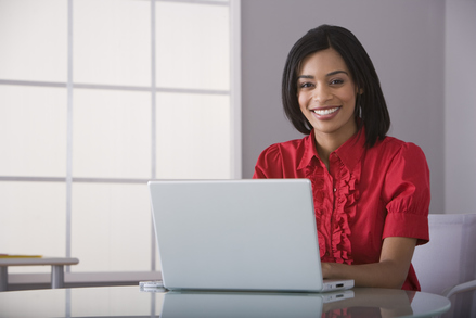 Image: Woman smiling, sitting at a desk and typing on a computer